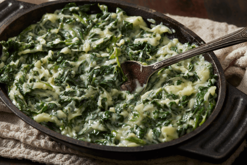 A black dish containing creamed spinach and a wooden spoon