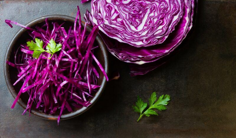 A black bowl of shredded purple cabbage, next to half a purple cabbage