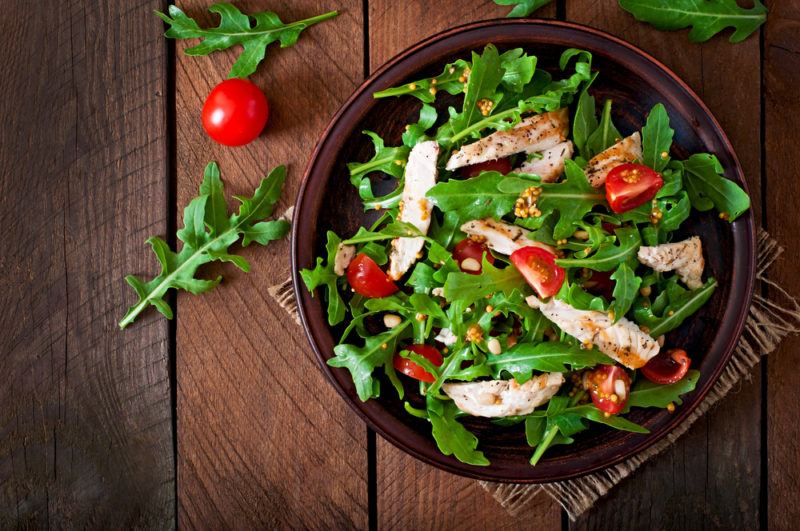 A large bowl that contains a fresh salad with chicken and tomatoes