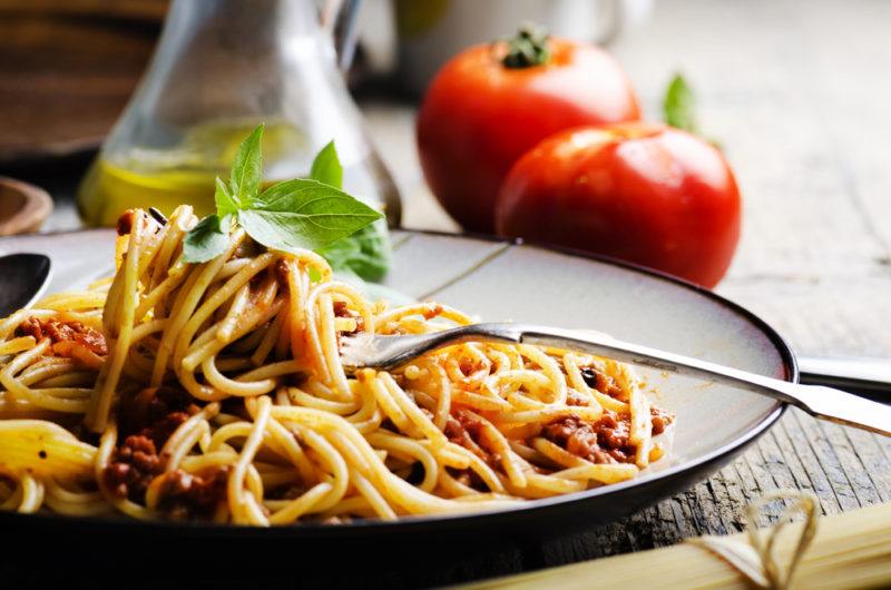 A black bowl with fresh pasta from a restaurant, with tomatoes and olive oil in the background