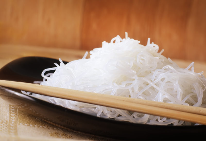 A black dish with cooked rice noodles and chopsticks | Food For Net A black dish with cooked rice noodles next to chopsticks