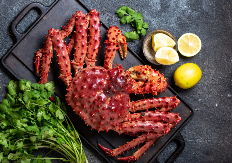 A fresh Alaskan king crab on a slate next to greens and lemon wedges