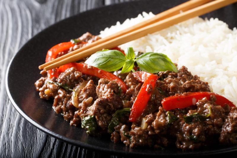 A black dish of pad gra prow and rice, with chopsticks