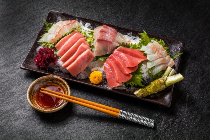 A black dish of sashimi next to a small bowl of dipping sauce and some chopsticks