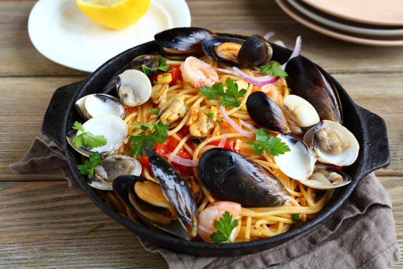 A fry pan with seafood pasta on a table