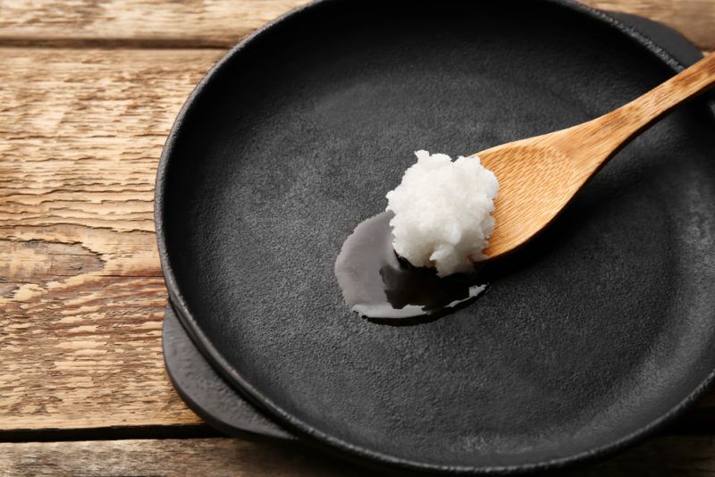 A black frypan with a wooden spoon containing olive oil on a wooden table