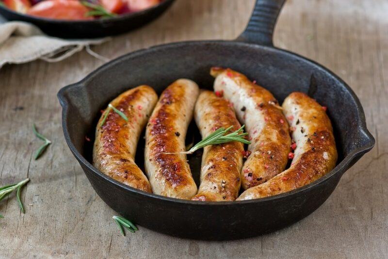 A cast iron frypan with five large cooked sausages