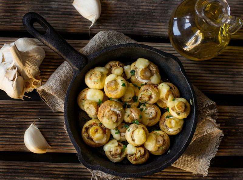 A black cast iron pan with cooked mushrooms and seasonings on a table