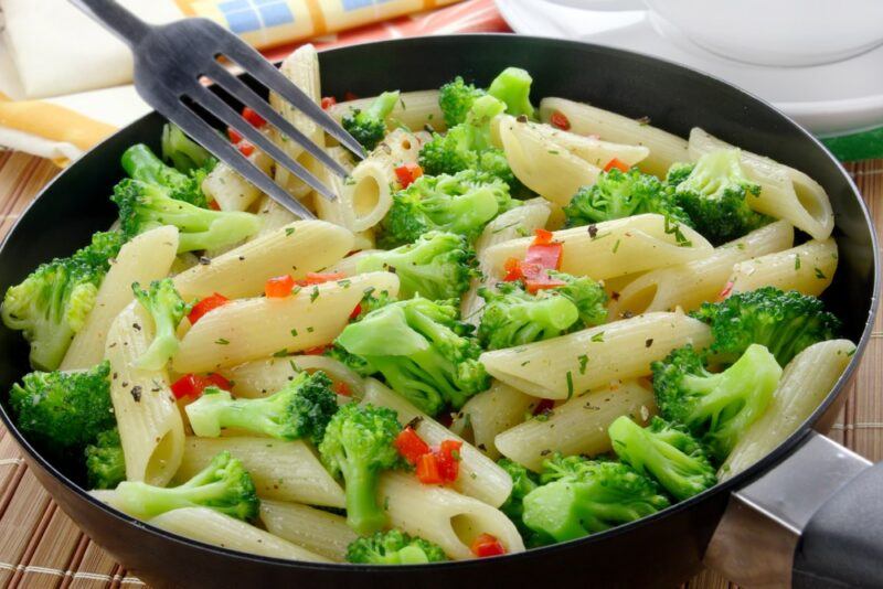 A black frypan with a pasta dish that includes broccoli and other fresh ingredients