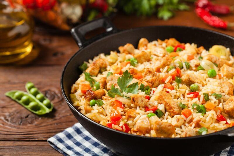 A black pan with fried rice and veggies on a wooden table with condiments and ingredients in the background