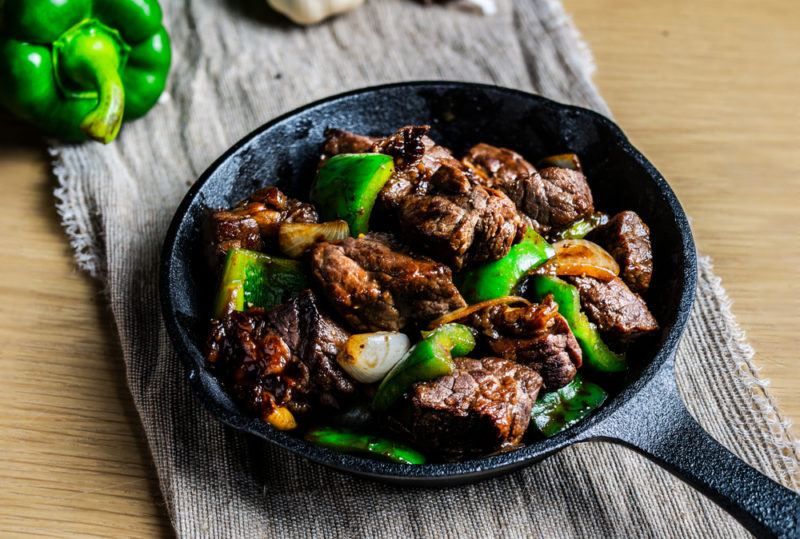 A black dish of shaking beef on a wooden table