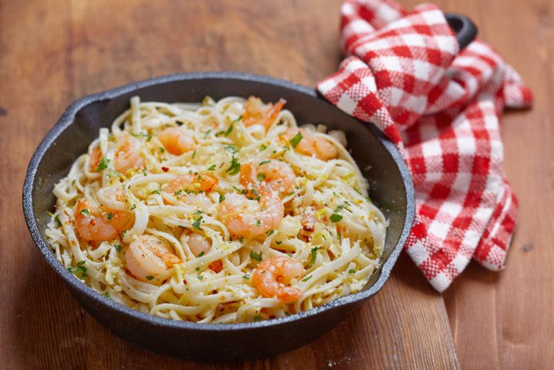 A black frypan filled with shrimp scampi with a red and white tea towel around the handle