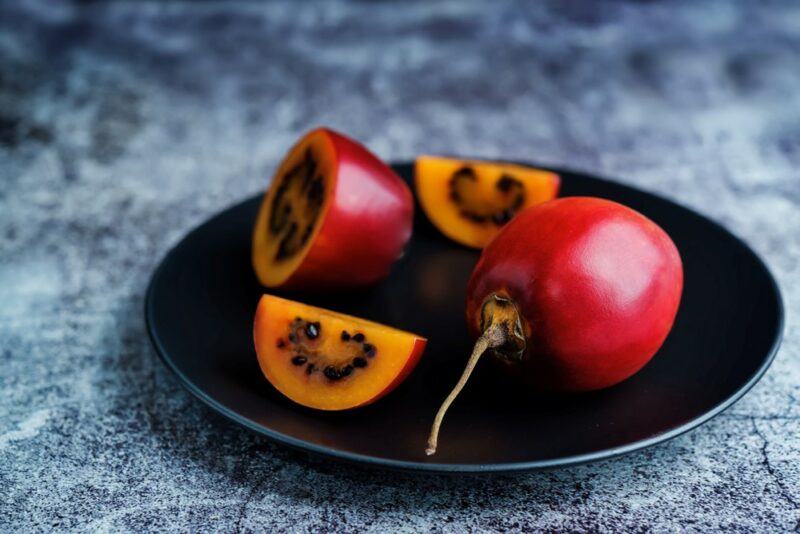 A black plate with a whole tamarillo, one half of the fruit, and a few wedges