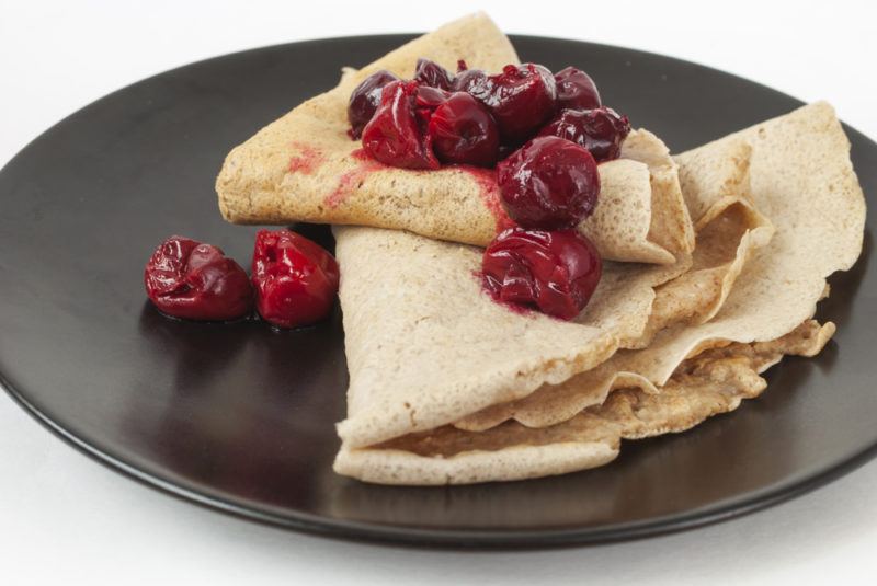 A black dish with buckwheat pancakes and berries