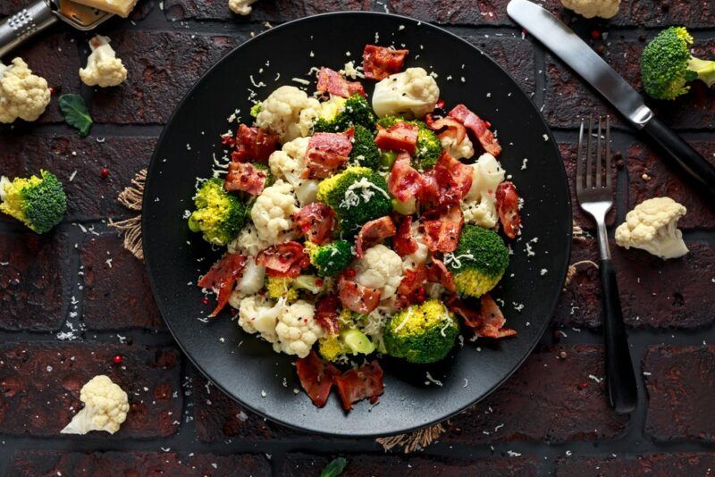 A black dish with a cauliflower, broccoli, and bacon salad