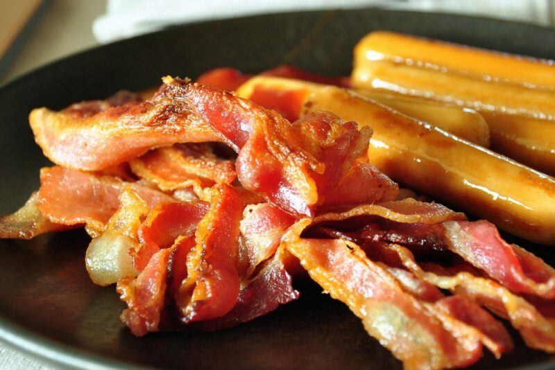 A black plate with sausages and bacon, as part of a Russian breakfast