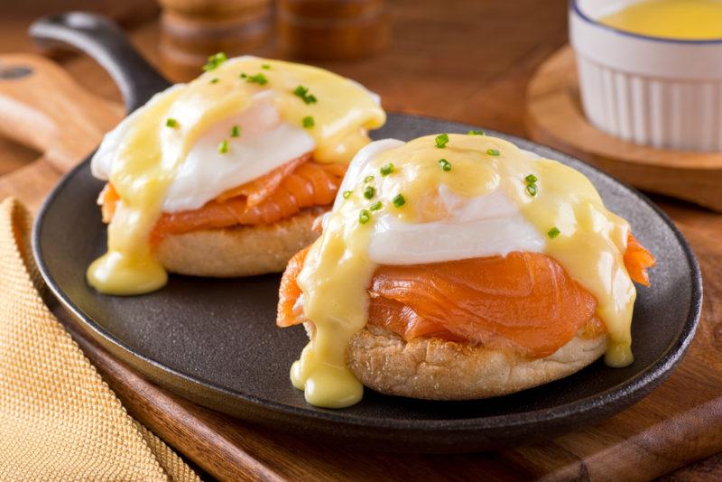 Two English muffins on a black plate, with smoked salmon, poacked eggs, and Hollandiase sauce