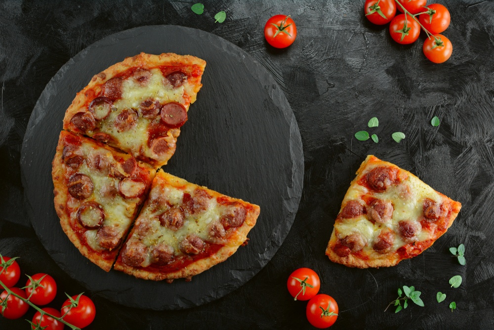 A black slate circle with fathead pizza and cherry tomatoes