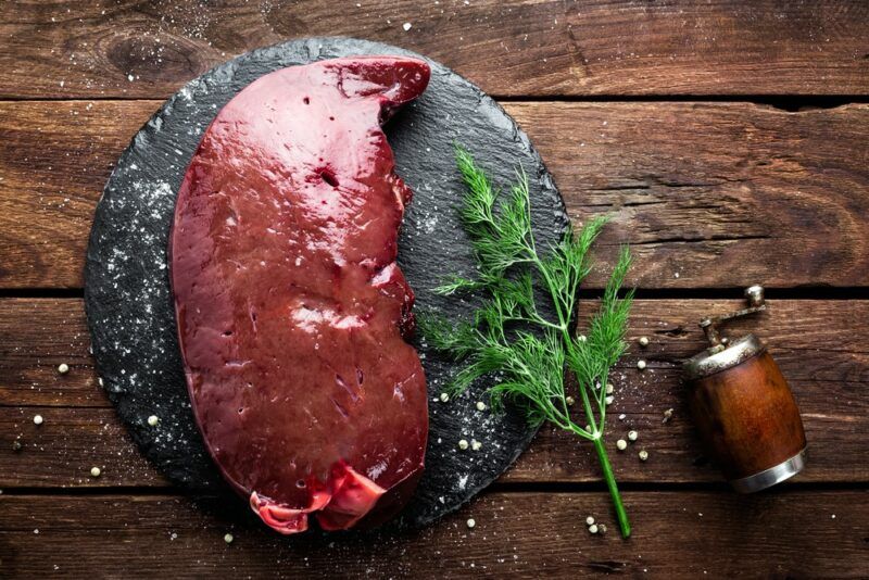 A wooden table with a black slab that contains a large piece of uncooked liver