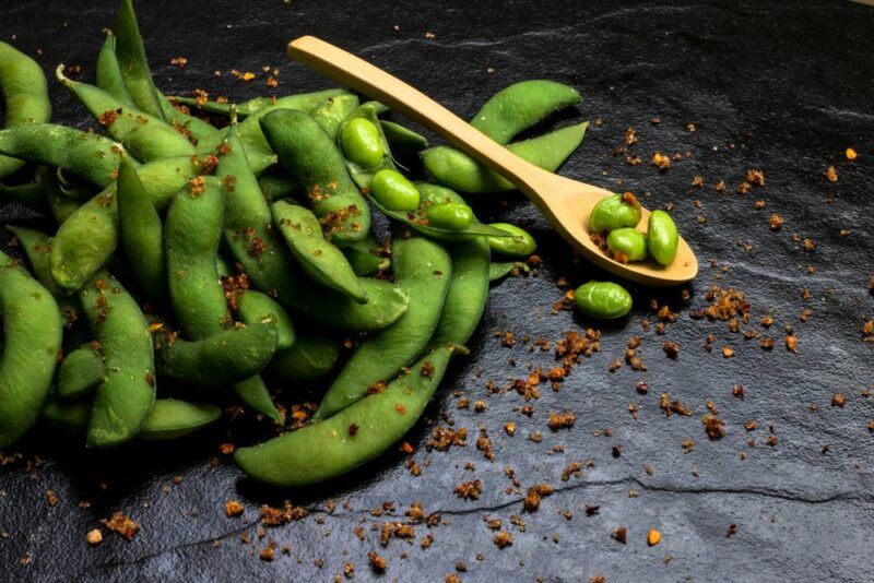 A selection of spiced edamame beans on a table with a couple of beans on a spoon