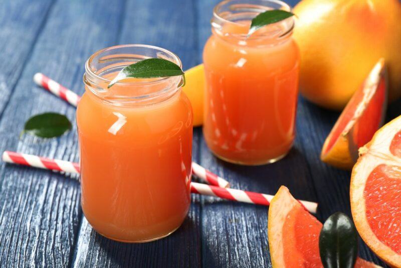 A wooden table with glasses of grapefruit juice, some straws, and some pieces of grapefruit