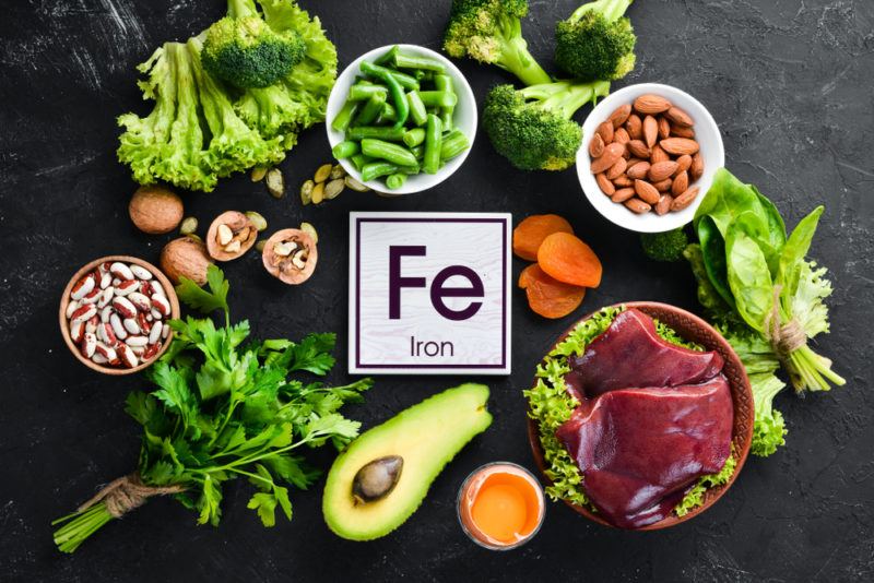 A black table with bright iron rich foods like greens and avocado, and the symbol for iron