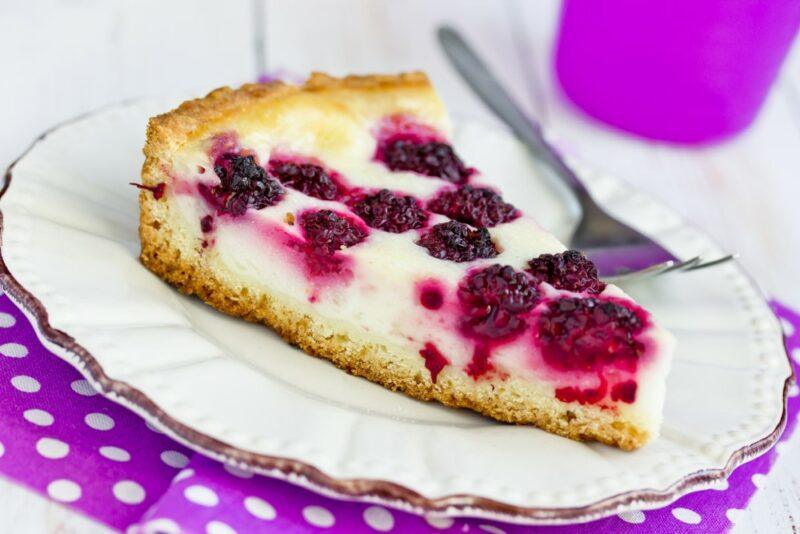 A white plate with a blackberry sour cream pie and a fork, on a purple and white piece of paper