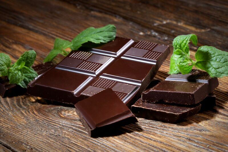 A wooden table with pieces of dark chocolate and mint leaves