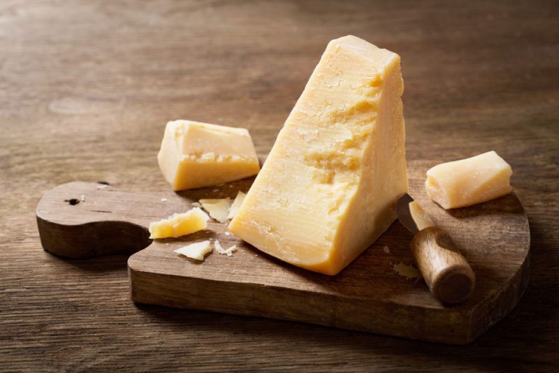 A block of parmesan cheese with smaller pieces on a cutting board