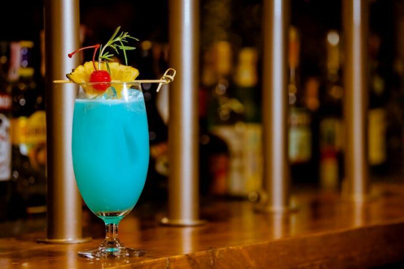 A creamy blue Hawaiian cocktail on a bar with many bottles in the background