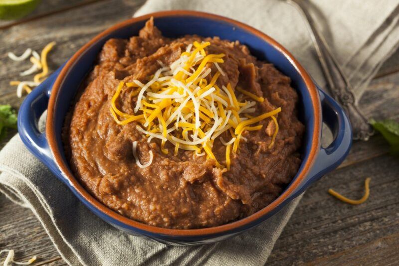 A blue and brown bowl of refried beans with cheese on top