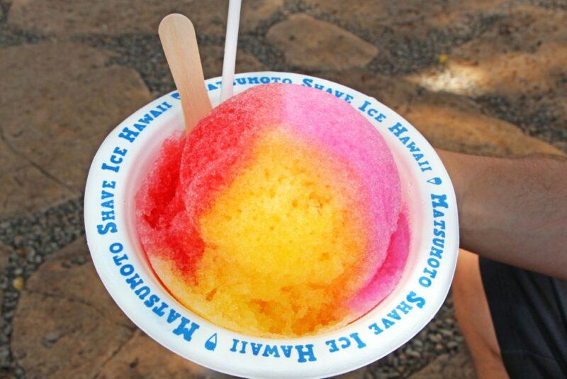 A white bowl with blue writing that contains a three-colored snow cone