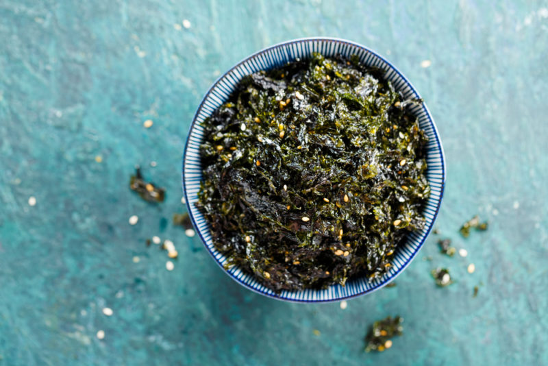 A blue and white bowl with small pieces of seaweed against a light blue background