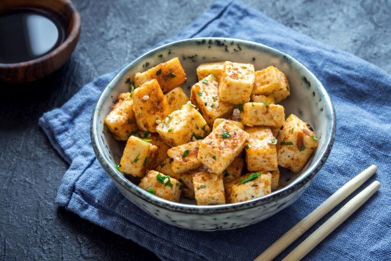 A blue and white bowl of tofu next to chopsticks | Food For Net A blue and white bowl of tofu next to chopsticks on a blue cloth with soy sauce in the background