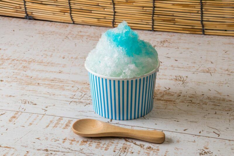 A blue and white paper container with a snow cone that has been topped with ocean breeze syrup