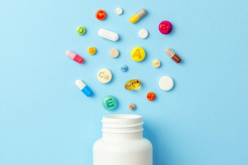 A white bottle against a blue background, with a variety of supplements around it