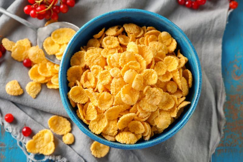 A blue bowl with fortified cornflakes, with more cornflakes spilled over the cloth