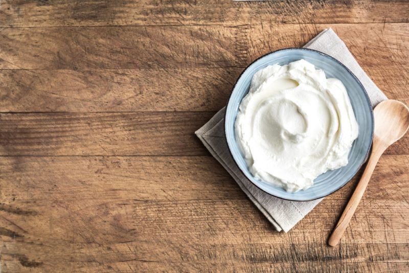 A blue bowl of yogurt with a spoon on a cloth that is on a wooden table