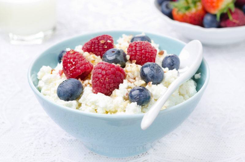 A blue bowl that contains cottage cheese topped with raspberries and blueberries