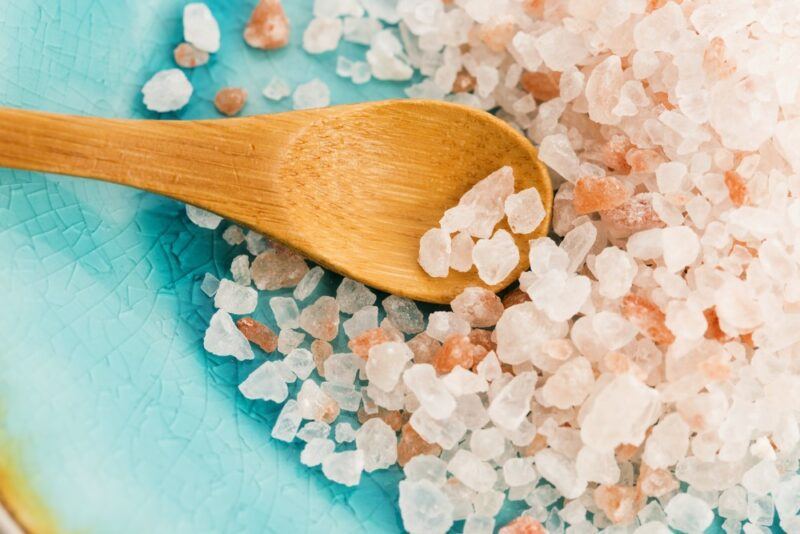 A light blue dish with a pile of coarse Himalayan salt and a wooden spoon