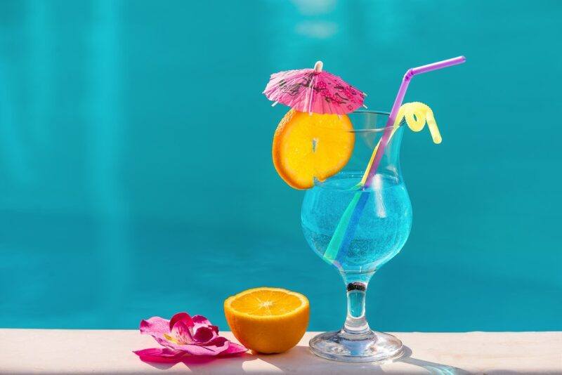 A light blue lagoon cocktail with bright garnishes in front of a pool