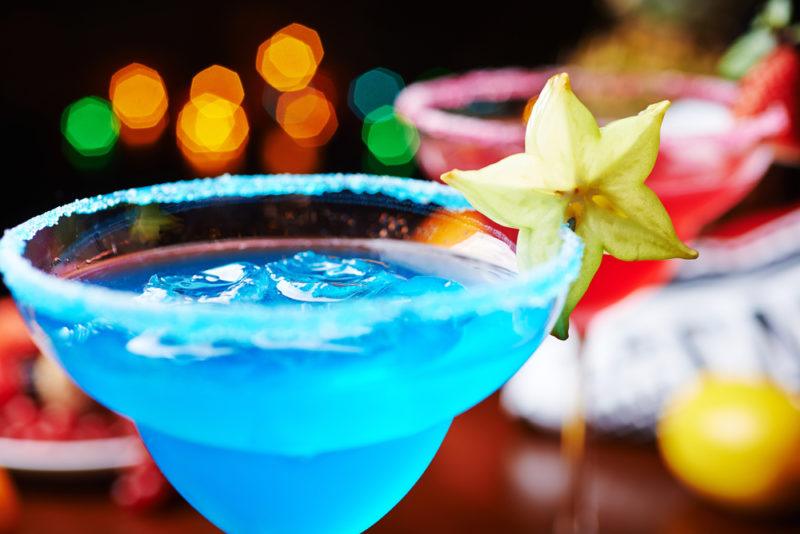 A blue margarita made using blue curacao in a cocktail glass with a strawberry daiquiri in the background