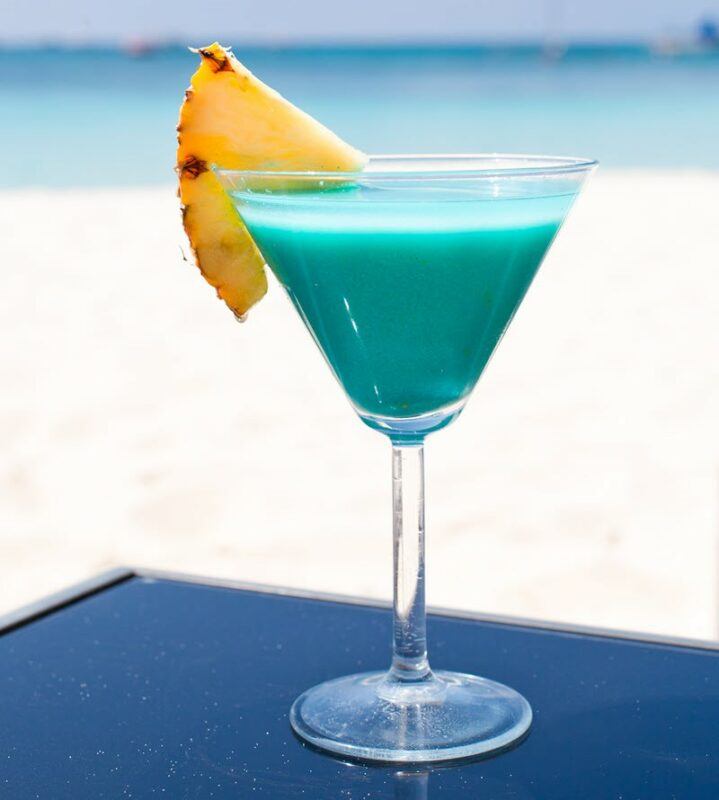 A light blue creamy cocktail called blue mood curacao and vodka, in front of a beach