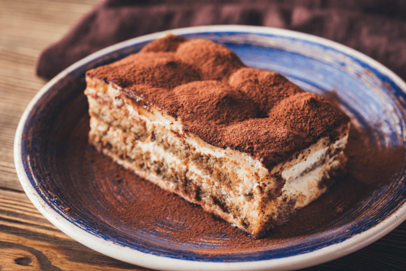 A blue and white plate of tiramisu that has been dusted with cocoa.