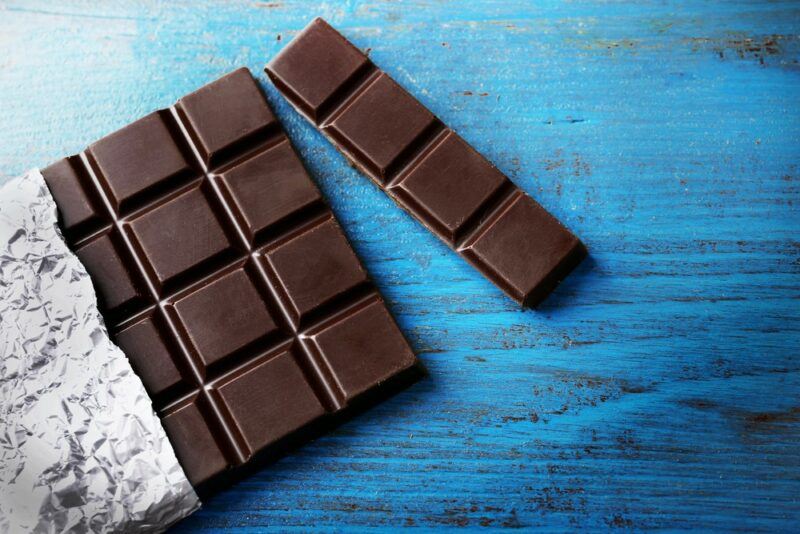 A blue table with a dark chocolate bar, where one piece has been separated from the rest.