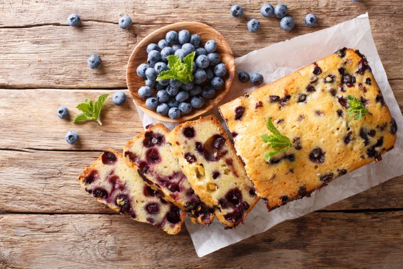 A blueberry fruit loaf on a wooden table or deck, next to a bowl of blueberries