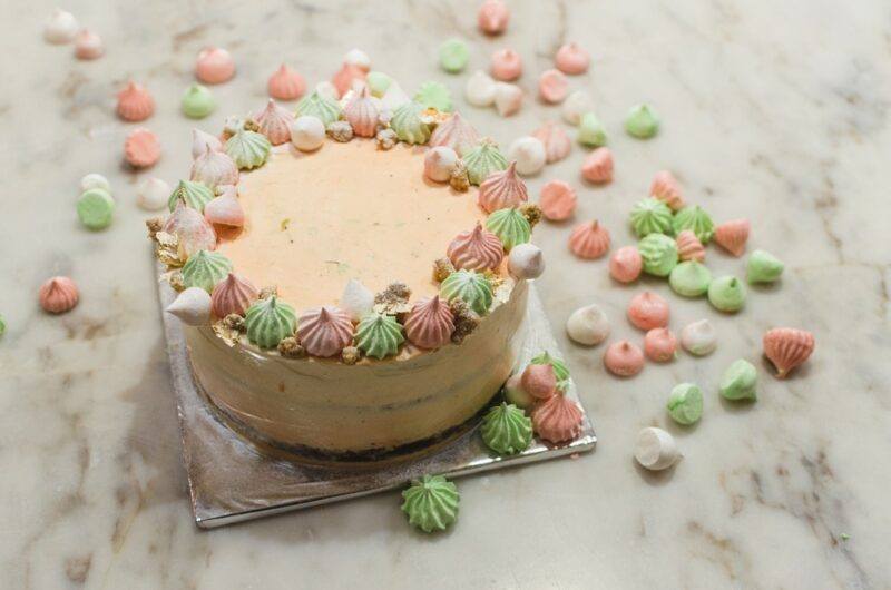 A glass board with an earl grey and lavender cake that has been topped with green, pink, and white meringues