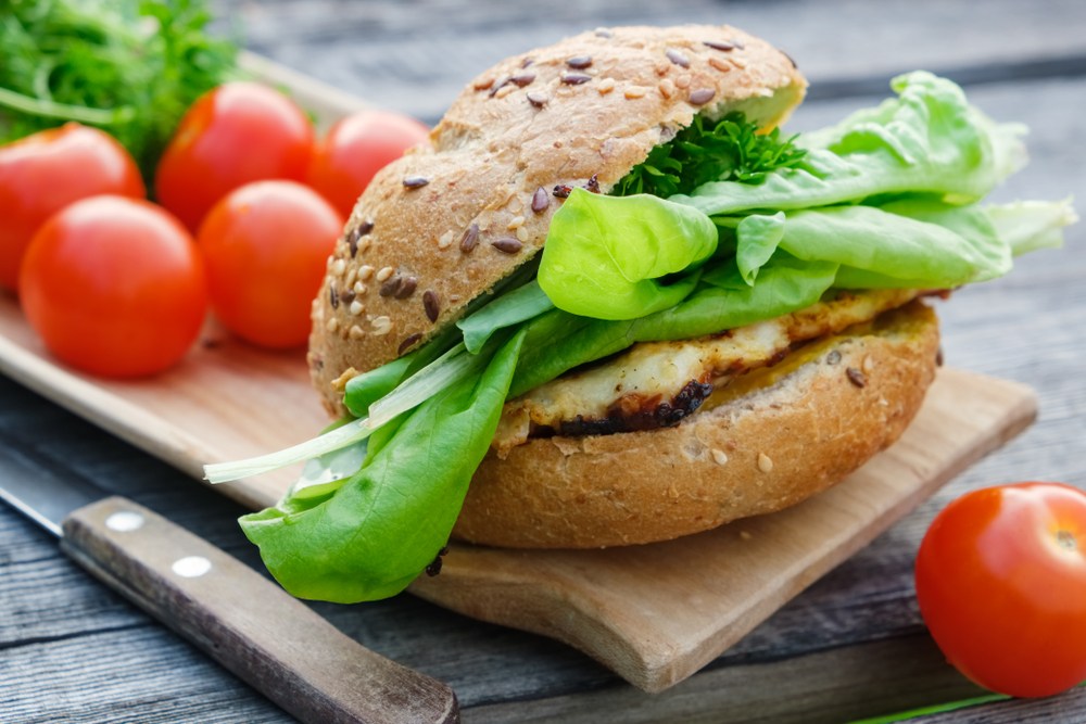 A small board with a fresh chicken burger with lettuce, next to some cherry tomatoes