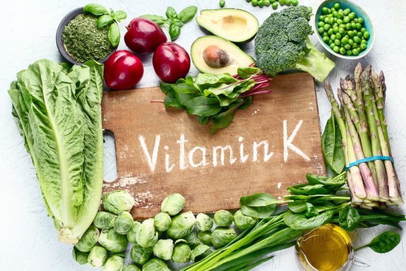 Vitamin K rich foods on a wooden table, including various types of greens