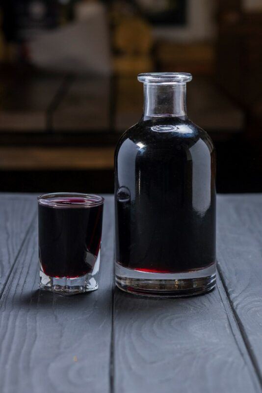 A bottle and a shot glass both containing Instant Pot root beer moonshine